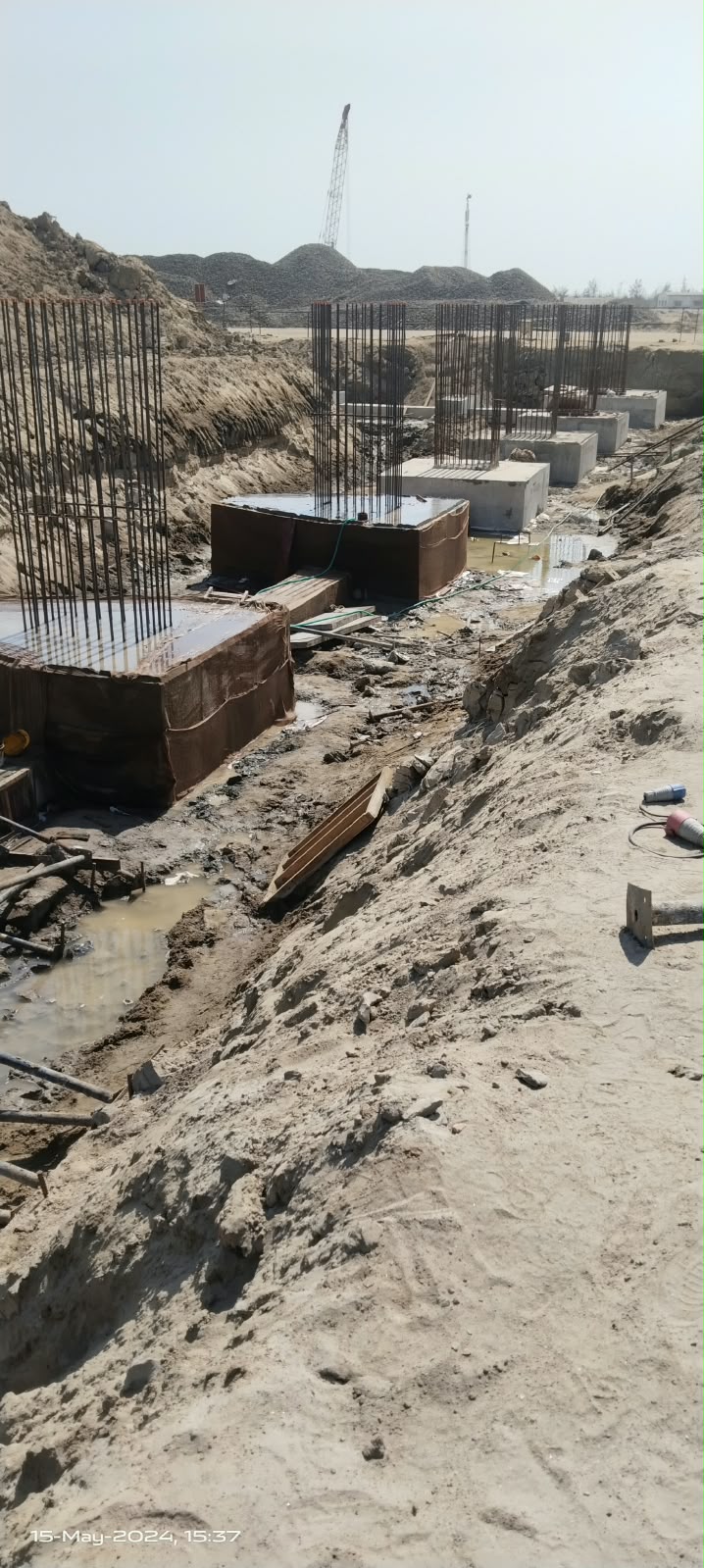 A row of cast concrete footings with reinforcement, beside an excavated trench